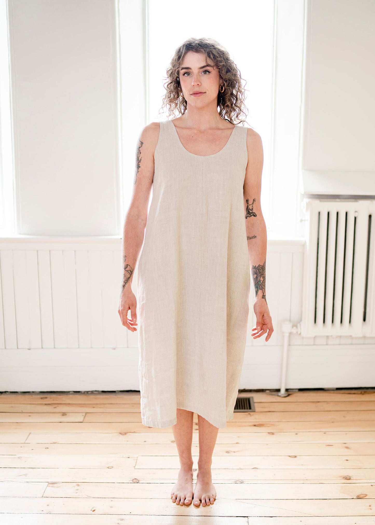 A girl wears a long linen sleeveless dress in an oatmeal colour. A girl wears a long mocha linen dress.