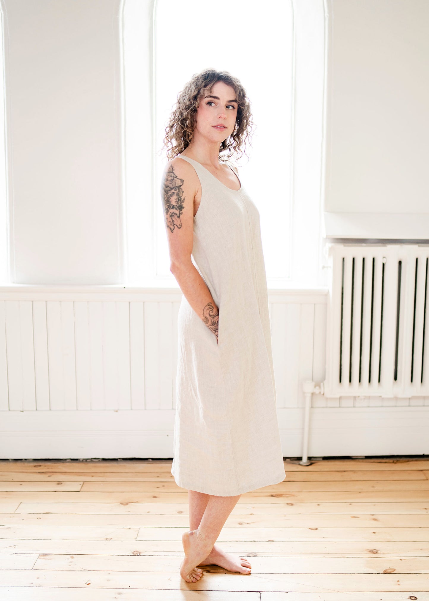 A girl wears a long linen sleeveless dress in an oatmeal colour. 