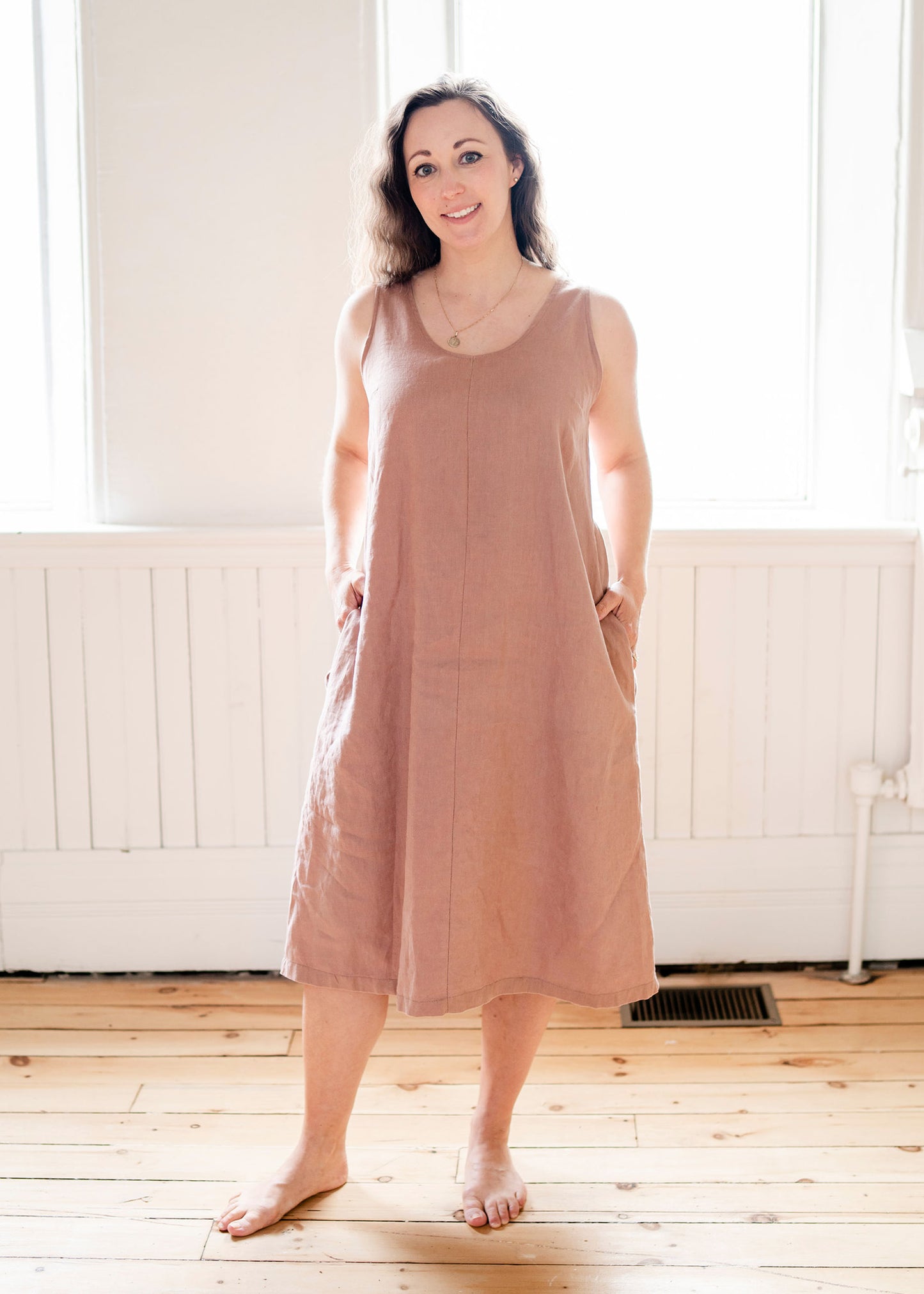  A girl wears a long sleeveless mocha coloured linen dress.